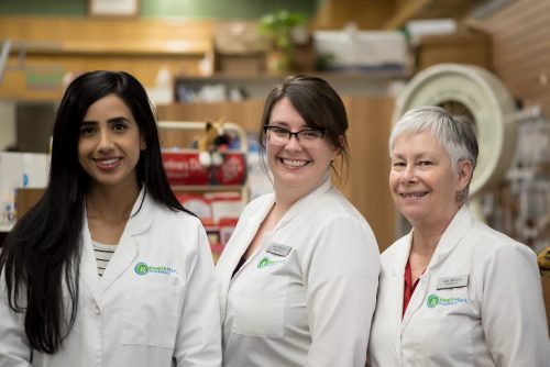 an image of 3 female pharmacists standing together in their white lab coats smiling for a photograph inside the Corner Drug Store
