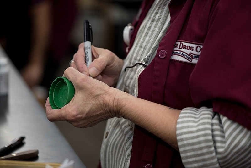 an image of a Corner Drug Co. employee in a red smock writing on a medicine bottle with a Sharpie pen.