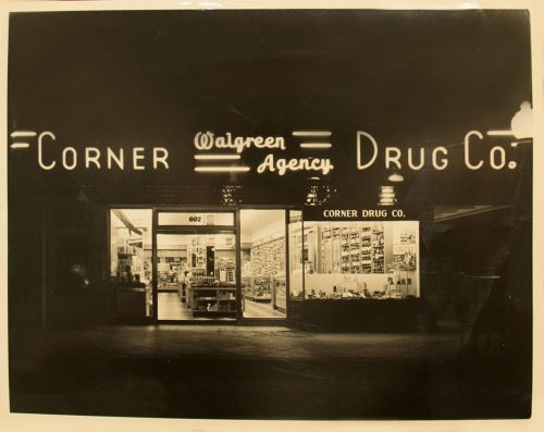 an old black and white photograph that has yellowed with age of the Corner Drug Company building after it was purchased and renamed