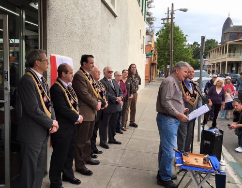 An image of some people standing together against a wall as another person speaks at a podium in front of them