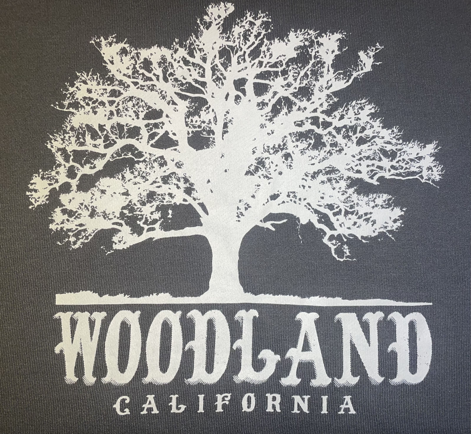 a closeup of a white Woodland logo featuring a silhouette of a large tree